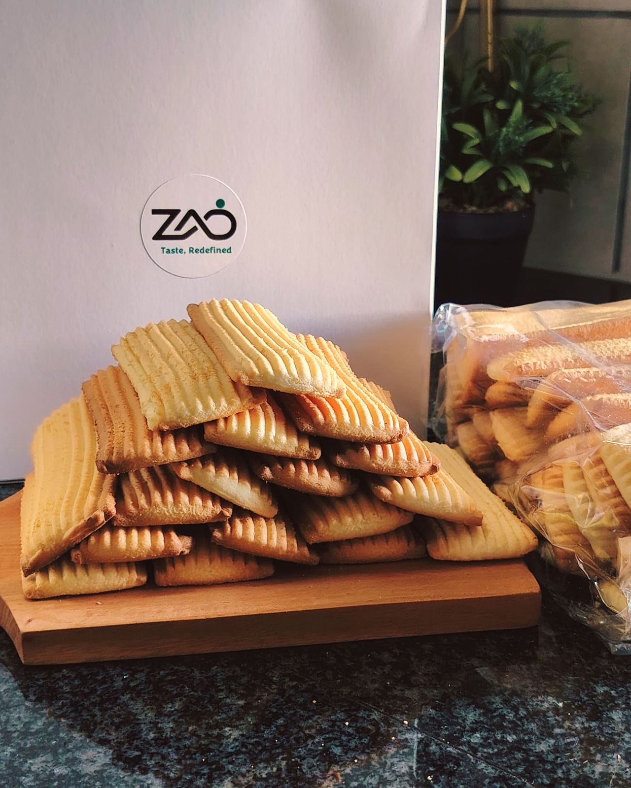 A stack of classic tea biscuits on a board in front of a Zad gift box, with a bag of biscuits beside it