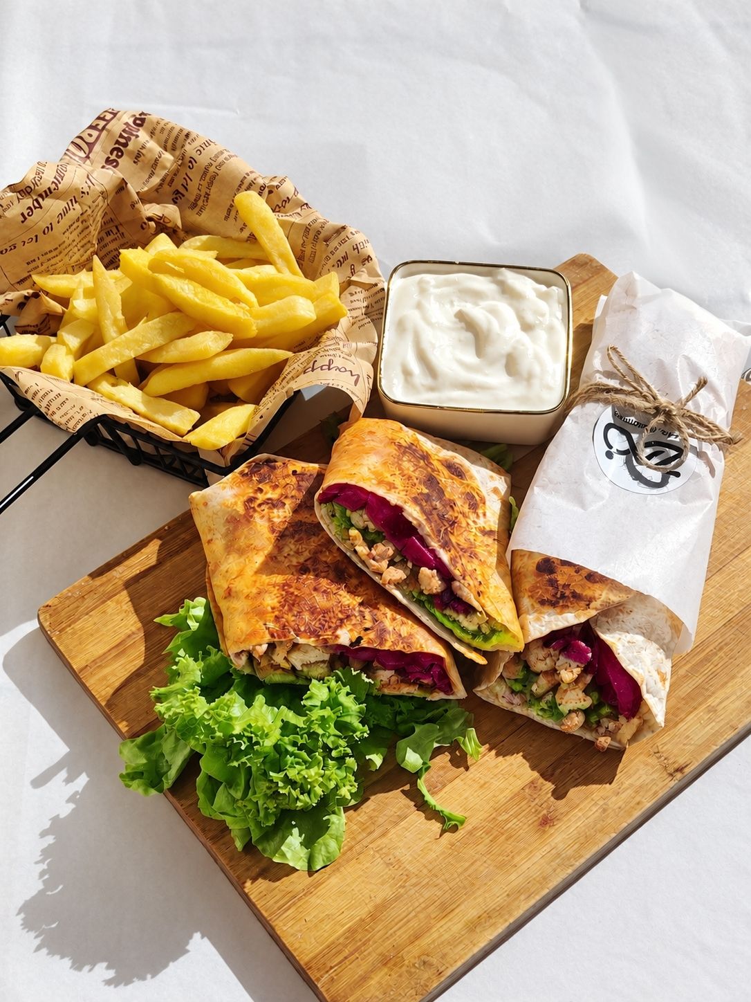 Chicken shawarma wraps with chips, lettuce and white sauce on a board