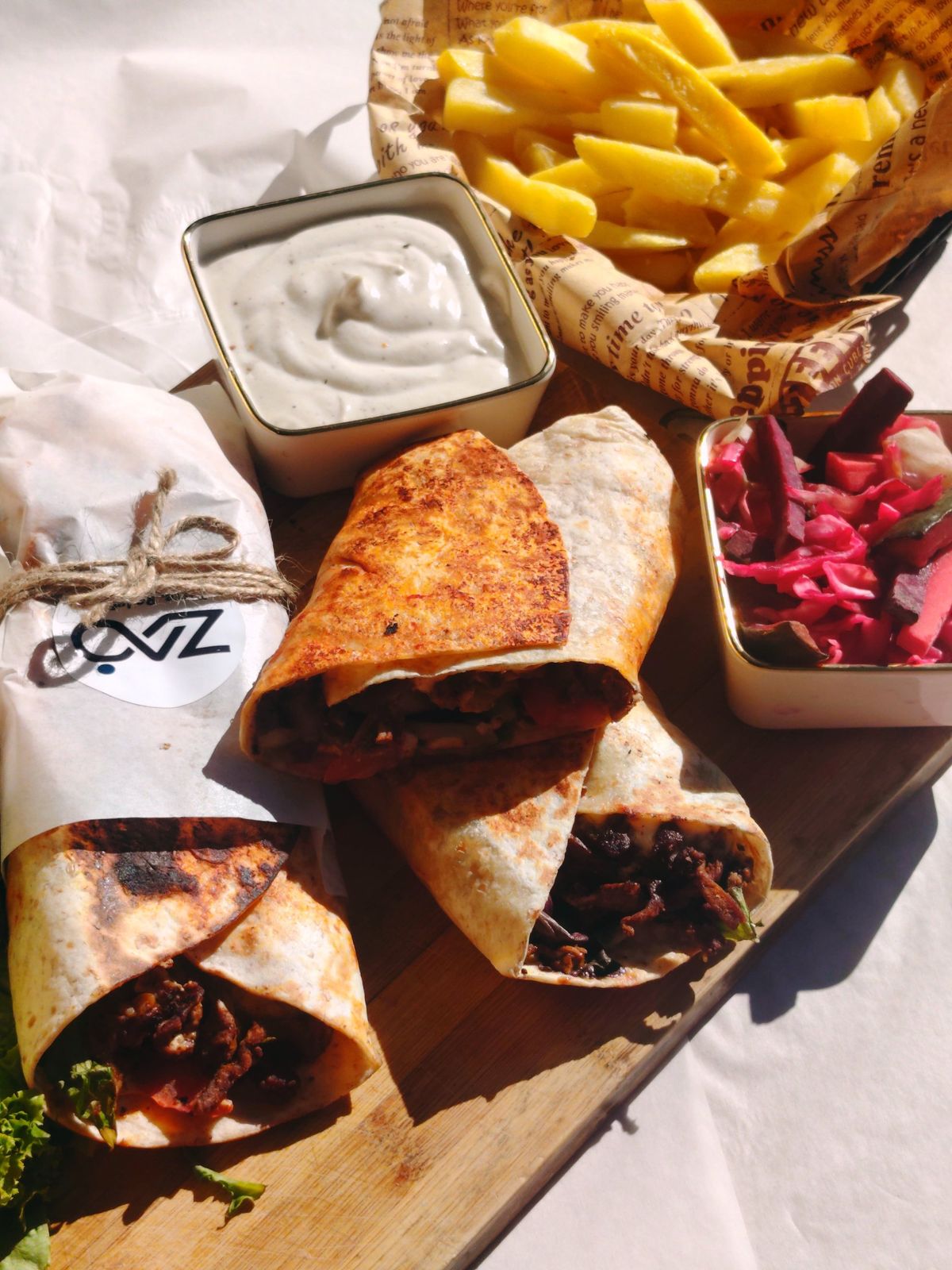 Beef shawarma wraps with chips, white sauce and pickled vegetables on a board