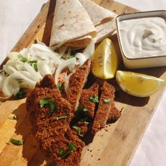 Aqashi with flatbread, sliced onion, lemon wedges and white sauce on a board